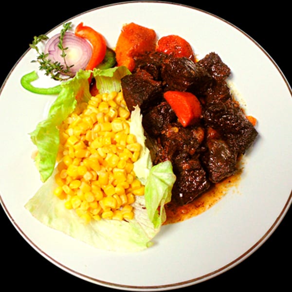 A plate of Jamaican stewed beef with corn, lettuce, red onion, and bell pepper.