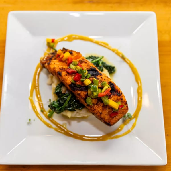 Grilled salmon with colorful diced peppers and mango, served over greens and mashed potatoes.