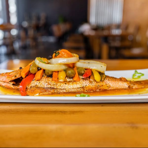 Whole fried Jamaican escovitch fish topped with colorful vegetables, onions, and sauce on a white plate.