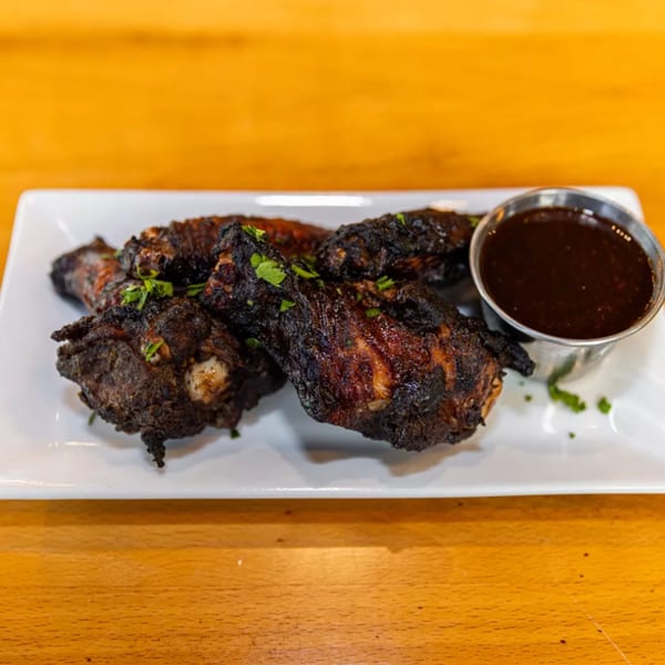 Charred Jamaican jerk chicken wings with fresh parsley and a side of dark dipping sauce.