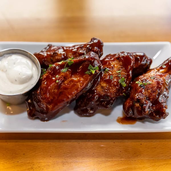 Five Jamaican jerk chicken wings with a side of ranch dressing on a white plate.