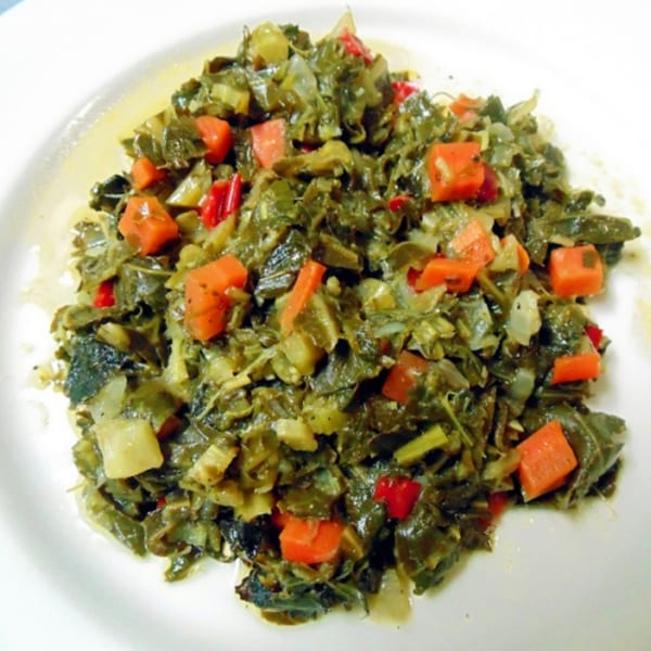 A close-up of Jamaican callaloo with diced carrots and red peppers on a white plate.