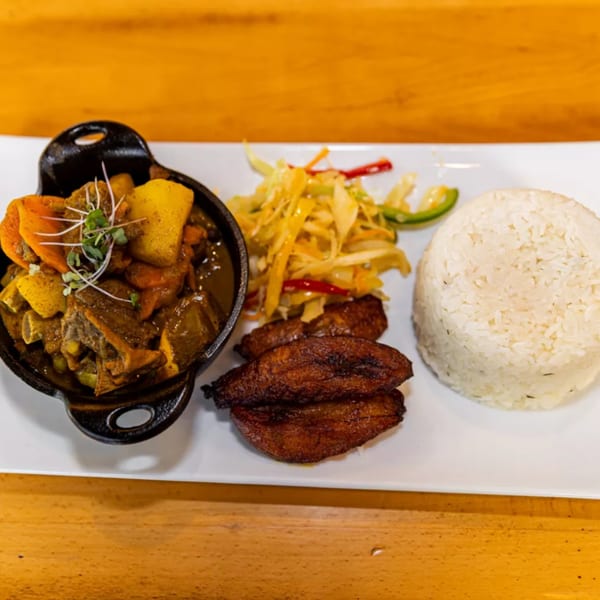 Jamaican curry chicken with rice, fried plantains, and coleslaw on a white plate.